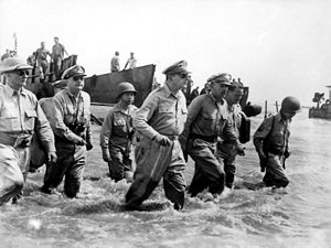 seven men in uniform wade through the surf.