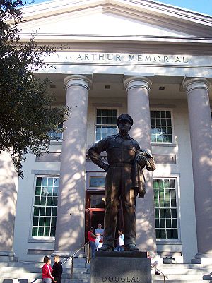 a large bronze statue of macarthur stands on a pedestal before a large white building with columns. an inscription on the building reads: 