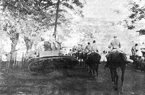 a long column of men on horseback moving down a road. a tank is parked beside the road.