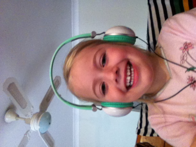 young girl, smiling, with headphones positioned over her ears.