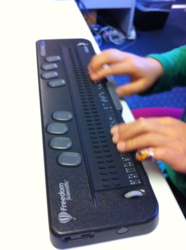 child\'s hands feel the braille on a refreshable braille display.