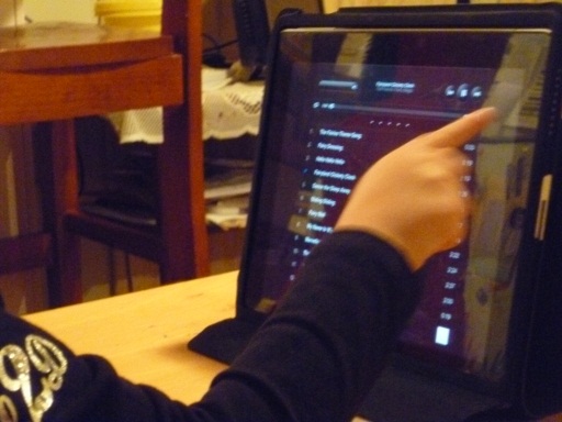 child uses pointer finger to select item on an ipad. the ipad has a high contrast setting, white text on a black background.