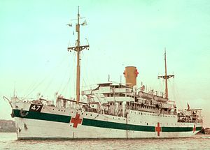 a single-funnelled merchant ship at rest. the ship is painted white, with a dark green horizontal band along the hull, interspersed by three red crosses. the number 