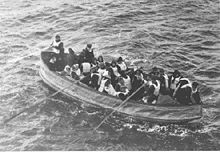 photograph of a lifeboat, filled with people wearing life jackets, being rowed towards the camera.