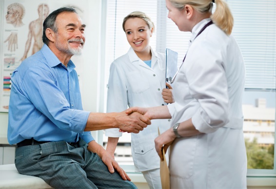 a male patient seated on an exam table in an exam room shakes hands with a female doctor