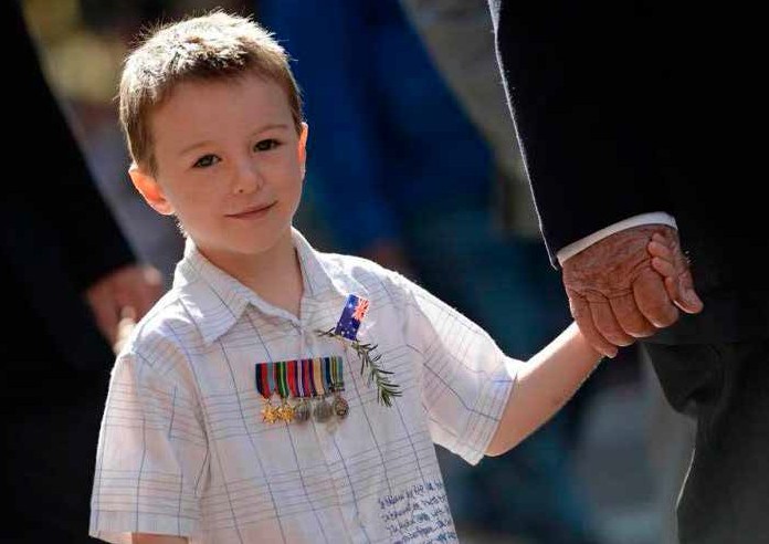 a child wearing medals holding onto a veterans hand.