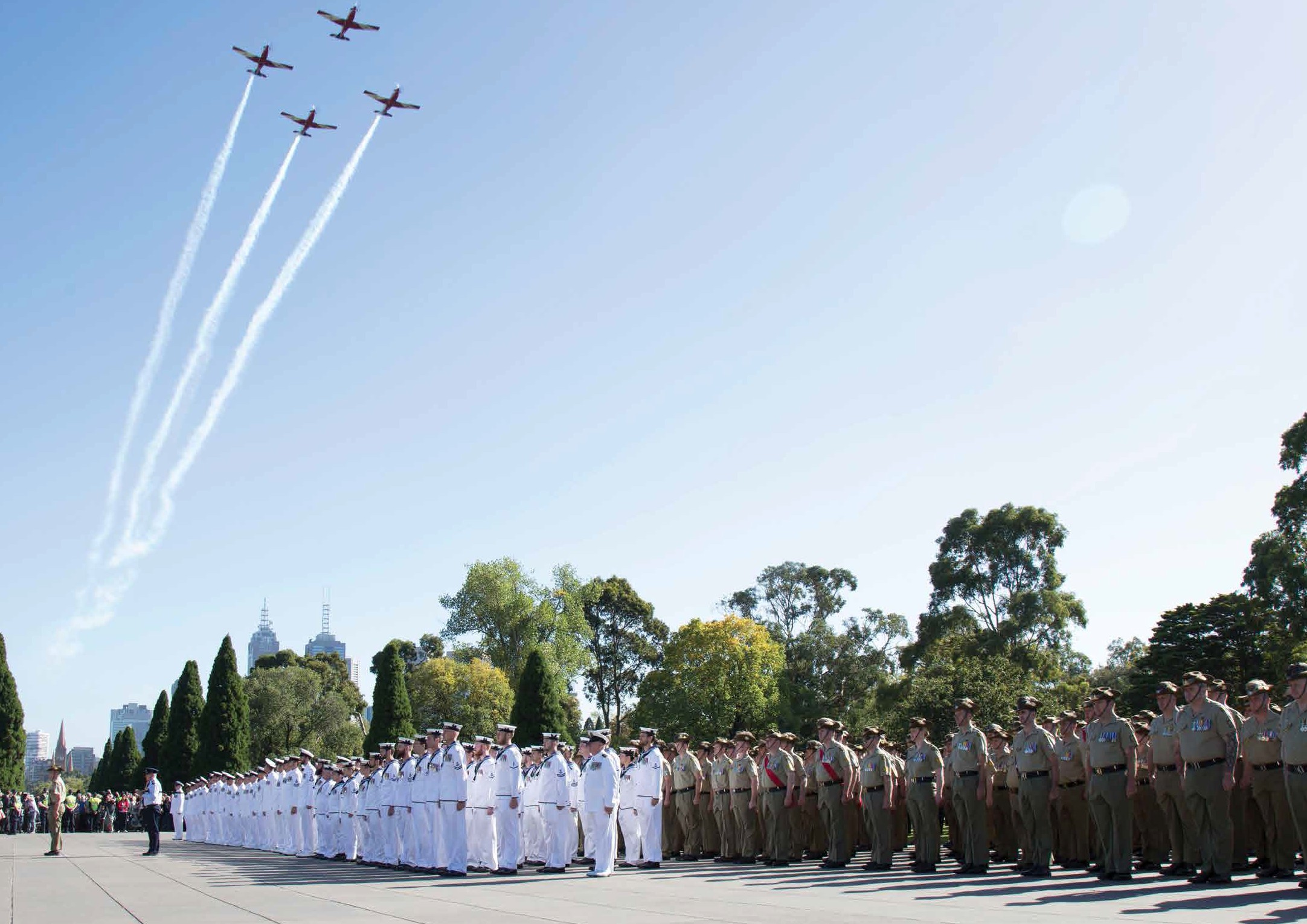 soldiers standing in formation with jets flying over head in a cross formation.