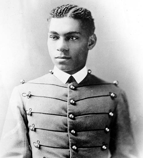 cadet henry o. flipper in his west point cadet uniform. it has three large round brass buttons left, middle and right showing five rows. the buttons are interconnected left to right and vice versa by decorative thread. he is wearing a starched white collar and no tie. he is a lighter-colored african american with plated corn rows of neatly done hair. he is facing the camera and looking to the left of the viewer.